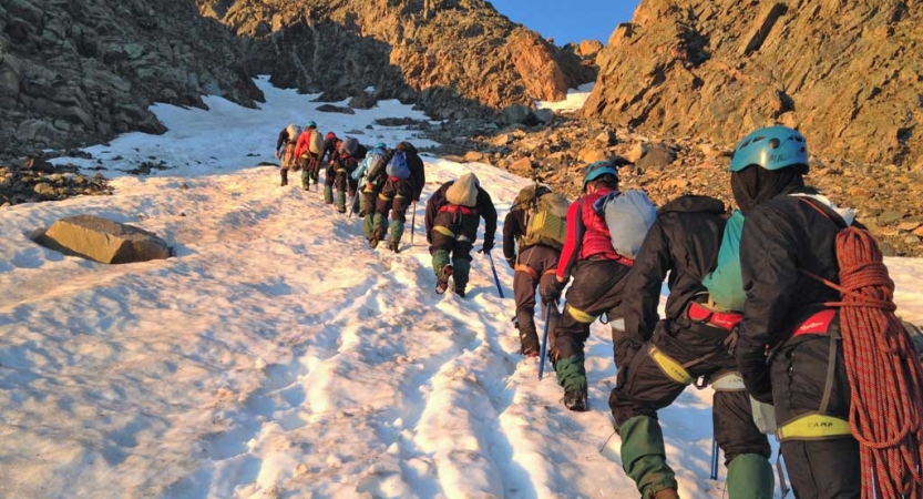 A group of people wearing safety gear hike up a snowy incline framed by rocks